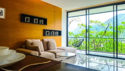 a living room with a couch and a large window at The Woods Natural Park Resort Phuket in Kamala Beach