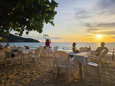 people sitting at tables on the beach at sunset at TT Naiyang Beach Phuket in Nai Yang Beach