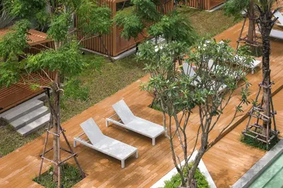 two white chairs and a wooden deck with trees at Andaman Embrace Patong, Phuket in Patong Beach