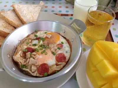 a bowl of food with eggs and bread and a glass of beer at Sandy House Rawai in Rawai Beach