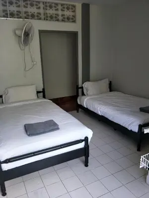 two beds in a room with a fan on the wall at Nit Guest House in Kata Beach
