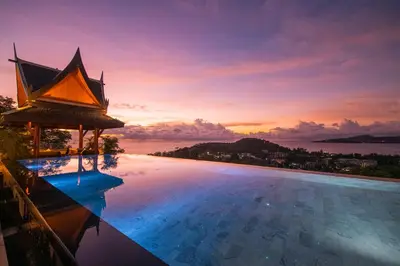 a pool with a view of the ocean at sunset at Baan Phu Prana Boutique Villa in Surin Beach
