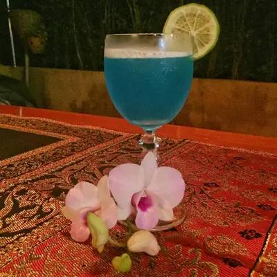 a glass with a blue drink and flowers on a table at Krabi Villa Phu Khao Private Resort in Klong Muang Beach