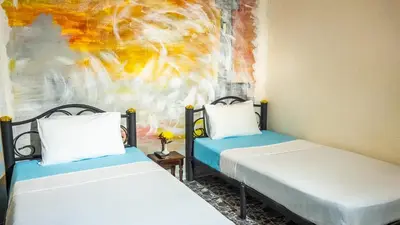 two beds in a room with a painting on the wall at Sabina Guesthouse Kamala in Kamala Beach