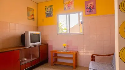 a room with a tv and a table and a window at Sabina Guesthouse Kamala in Kamala Beach