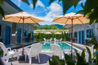 a swimming pool with white chairs and umbrellas at Ongsa House in Bang Tao Beach