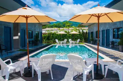 a swimming pool with white chairs and umbrellas at Ongsa House in Bang Tao Beach