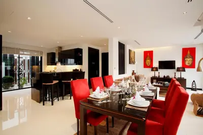 a dining room and living room with a table and red chairs at By The Lake Villas in Nai Harn Beach