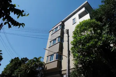 a tall white building with trees in front of it at Benjamas Place Hotel in Rawai Beach