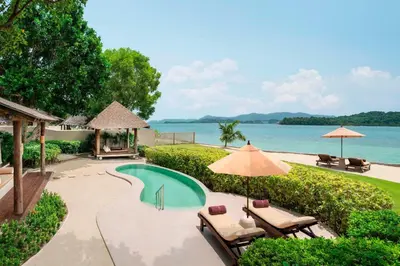 a swimming pool with chairs and umbrellas next to the water at The Naka Island, a Luxury Collection Resort & Spa, Phuket in Ko Naka