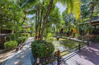 a garden with a pond and palm trees at Princess Kamala Beachfront Hotel - SHA Extra Plus in Kamala Beach