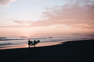two people walking on the beach with their surfboards at Sleep Box Patong Hostel in Patong Beach