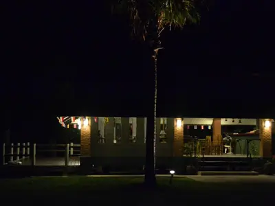 a palm tree in front of a building at night at Phuket Campground in Mai Khao Beach