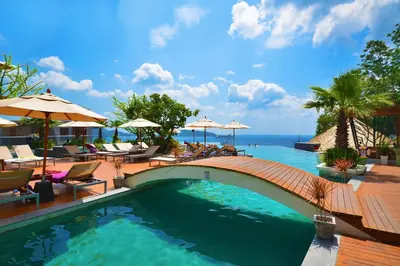 a swimming pool with a wooden bridge and the ocean at Kalima Resort and Spa in Patong Beach