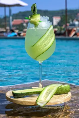a drink with a cucumber slice in a glass next to a pool at Zenseana Resort & Spa - Patong, Phuket in Patong Beach