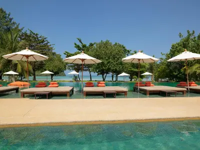 a pool with benches and umbrellas in the water at PP Charlie Beach Resort in Phi Phi Don