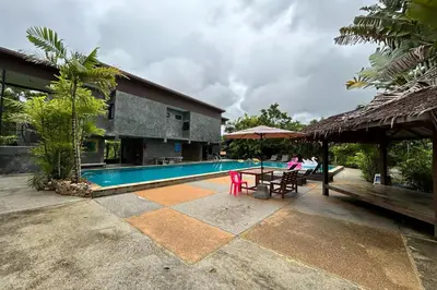 a woman sitting at a table next to a swimming pool at Tann Anda Resort in Thalang