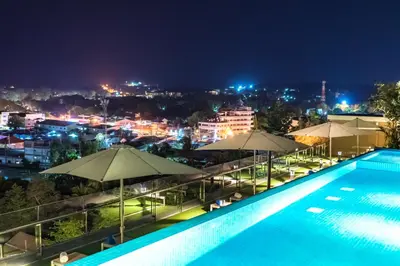 a pool with umbrellas and a city at night at Babylon Sky Garden in Rawai Beach