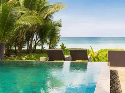 a swimming pool with two chairs and the beach at Infinity Blue Phuket by Elite Havens in Natai Beach