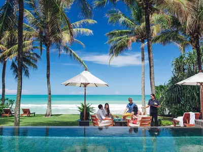 a group of people sitting around a table by the beach at Villa Nandana by Elite Havens in Natai Beach