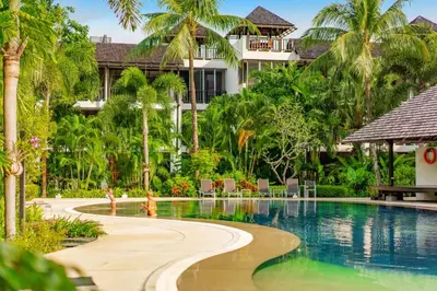 a resort swimming pool with palm trees and a building at Bangtao Beach Garden by RESAVA in Bang Tao Beach