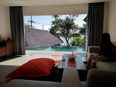 a woman sitting on a couch in a living room with a large window at JJ Queen Villa and Spa Kohyaonoi in Ko Yao Noi