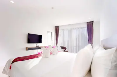 a white bedroom with a large white bed and a tv at Phoenix Hotel Karon Beach in Karon Beach