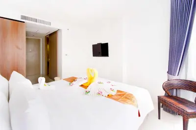 a white bedroom with a bed and a chair at Phoenix Hotel Karon Beach in Karon Beach