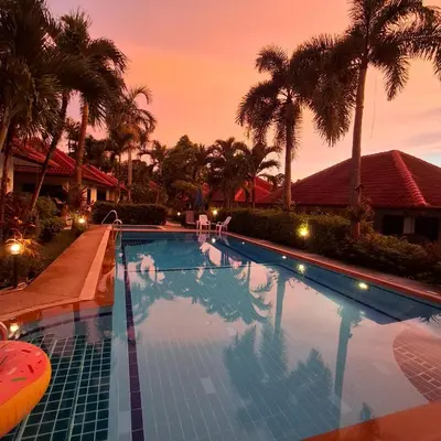 a swimming pool with palm trees and a sunset at D&K Smiley Phuket Resort in Rawai Beach
