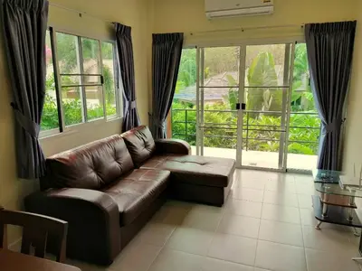 a living room with a brown leather couch and windows at Twin Villa in Ban Muang Mai