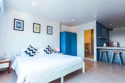 a bedroom with a large white bed and a kitchen at Maikhao Hotel, Phuket in Mai Khao Beach