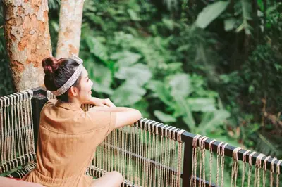 a woman sitting on a fence in a forest at Nua Tone Resort Bang Tao & Cafe in Bang Tao Beach