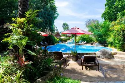 a swimming pool with a red umbrella and chairs and a table at Palm Garden Resort in Rawai Beach
