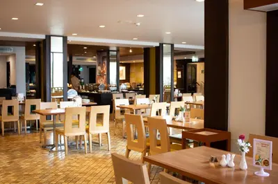 a restaurant with wooden tables and chairs and a cafeteria at Phuket Merlin Hotel in Phuket Town