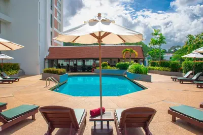 a swimming pool with an umbrella and chairs and a hotel at Phuket Merlin Hotel in Phuket Town