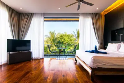 a bedroom with a bed and a television and a balcony at Amazing 5br, Seaview private PoolVilla by Intira Villas in Rawai Beach