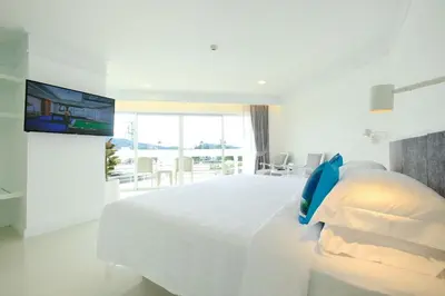 a white bedroom with a large bed and a tv at Andaman Beach Suites Hotel, Patong Phuket in Patong Beach