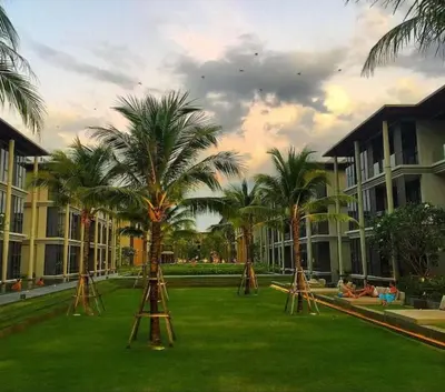 a lawn with palm trees in front of buildings at Baan mai khao apartment in Mai Khao Beach