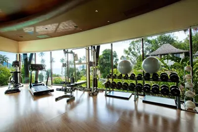 a gym with a lot of exercise equipment and windows at The Vijitt Resort Phuket - SHA Extra Plus in Rawai Beach