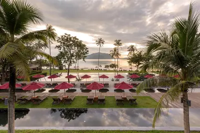 a pool with tables and red umbrellas and palm trees at The Vijitt Resort Phuket - SHA Extra Plus in Rawai Beach