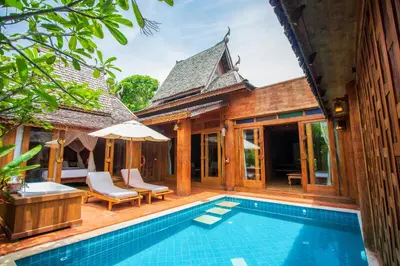 an outdoor pool with chairs and an umbrella next to a house at Santhiya Phuket Natai Resort & Spa in Natai Beach