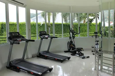 a gym with three tread machines in a room with windows at The Palmery Resort in Kata Beach