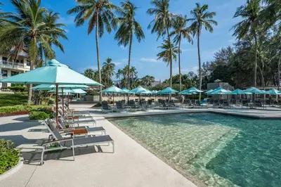 a pool with chairs and umbrellas and palm trees at SAii Laguna Phuket in Bang Tao Beach