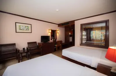 a bedroom with two beds and a desk and a window at Baumanburi Hotel Patong in Patong Beach