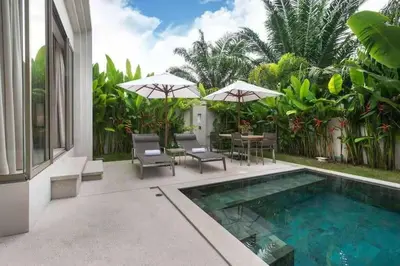 a swimming pool with chairs and umbrellas next to a house at Trichada Tropical in Bang Tao Beach