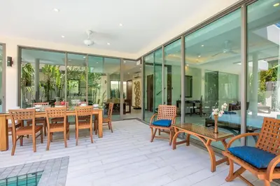 a patio with wooden tables and chairs and glass walls at VILLA Bangka 4BR Private pool villa Rawai in Rawai Beach