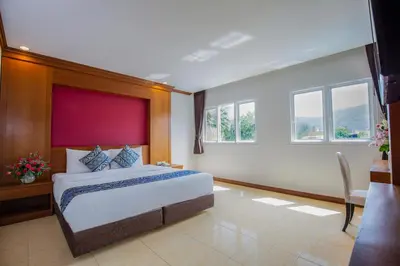 a bedroom with a bed and a desk and windows at Sungthong Kamala Beach Resort in Kamala Beach