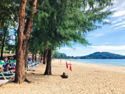 a beach with people sitting on chairs and trees at Beautiful 3br 380sqm Pool Villa Walk To Bangtao Beach and Catch club in Bang Tao Beach