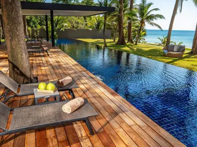 a resort swimming pool with chairs and the ocean at Grand Villa Noi in Natai Beach