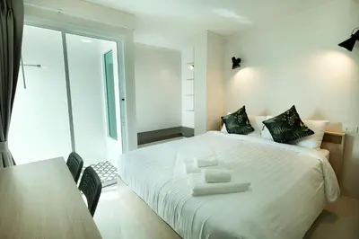 a bedroom with a white bed with a table and chairs at beHOME Phuket in Nai Yang Beach